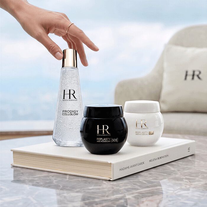Drei Helena Rubinstein Hautpflegeprodukte (Prodigy Cellglow und Re-Plasty) auf einem weißen Buch vor einem Fenster mit Blick auf eine Landschaft.​
