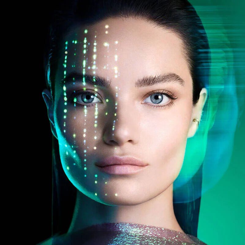 eine Frau mit dunklem Haar und blauen Augen, den Blick geradeaus gerichtet, vor einem grunen Hintergrund