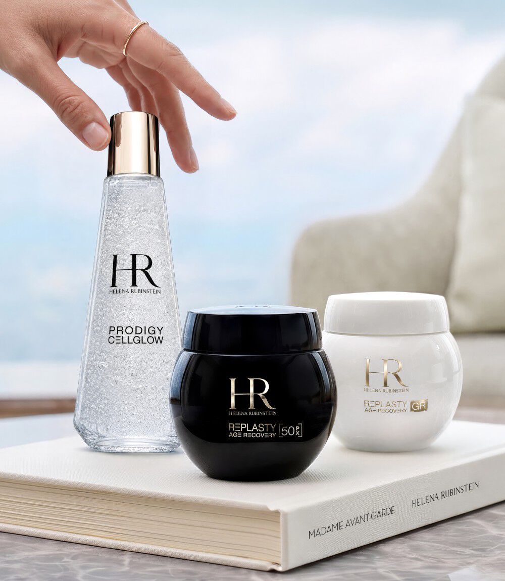 Drei Helena Rubinstein Hautpflegeprodukte (Prodigy Cellglow und Re-Plasty) auf einem weißen Buch vor einem Fenster mit Blick auf eine Landschaft.​