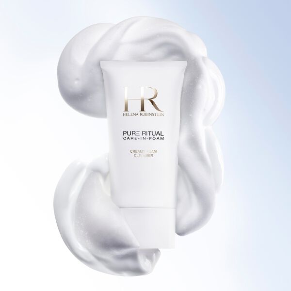 Nahaufnahme des Helena Rubinstein Pure Ritual Care-in-Foam Cleansers, umgeben von cremigem weißem Schaum, neben dem Gesicht einer Frau mit reinem und strahlendem Teint.​