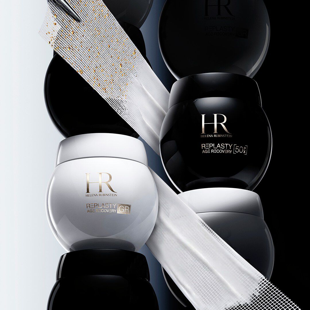 An artistic, high-end skincare composition featuring multiple stacked jars of Helena Rubinstein Replasty Age Recovery creams. 